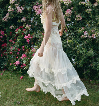 Woman in a white lace dress standing in a garden with pink flowers