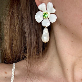 Close-up of a woman wearing a white floral earring with a pearl and green gemstone.