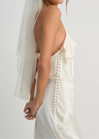 Woman wearing a white wedding dress with a veil against a plain background