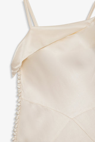 Close-up of a beige satin dress with thin straps and a textured edge on a white background