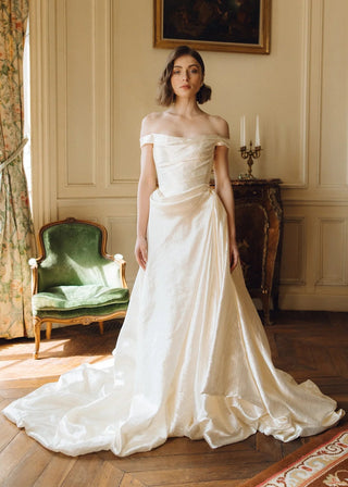 Woman in a white wedding dress standing in an elegant room with a painting on the wall.
