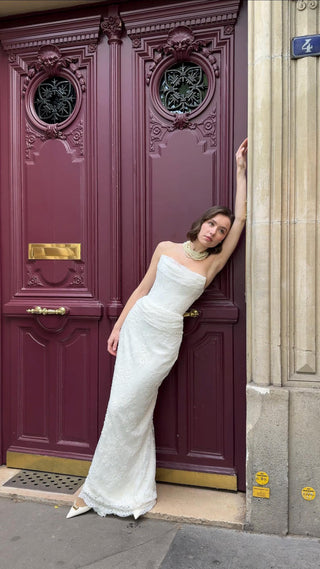 Woman in a white dress leaning against a purple door with decorative elements.