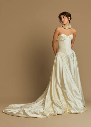 Woman wearing a strapless wedding dress with a long train on a beige background