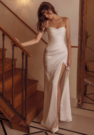 Woman in a white strapless gown with a high slit standing on a staircase.
