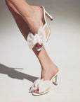 White high-heeled shoes with bow details on a neutral background