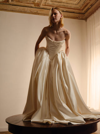 Woman in a white strapless gown standing in a softly lit room.