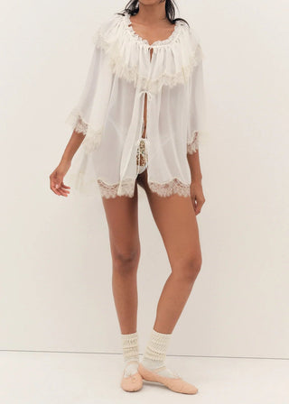 Woman wearing a white lace outfit with a sheer overlay on a white background