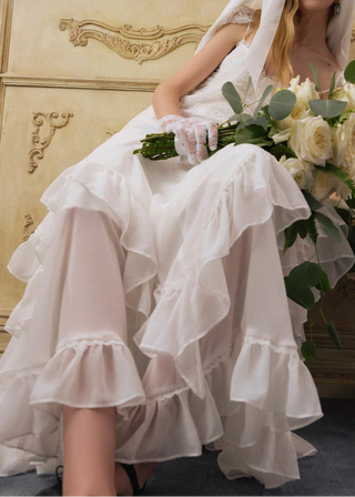 Woman in a white wedding dress holding a bouquet in an ornate room.