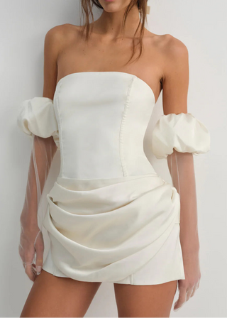 Woman wearing a white strapless dress with puff sleeves against a plain background - serene mini dress
