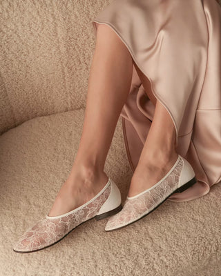 White lace flats worn with a pink satin skirt on a beige carpet.