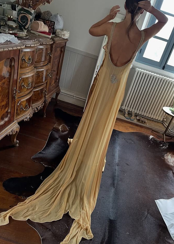Woman in a long, flowing dress standing in a room with wooden furniture and a radiator.