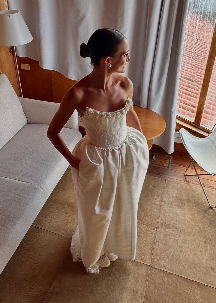 Woman in a white dress standing in a room with a large window and light-colored curtains.