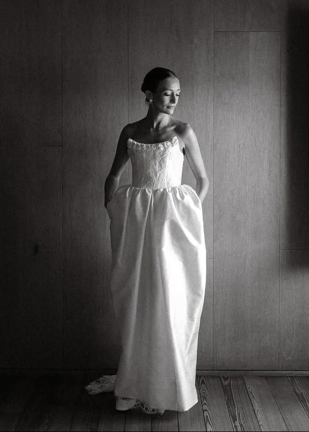 Woman in a white dress standing in a dimly lit room with a wooden floor.